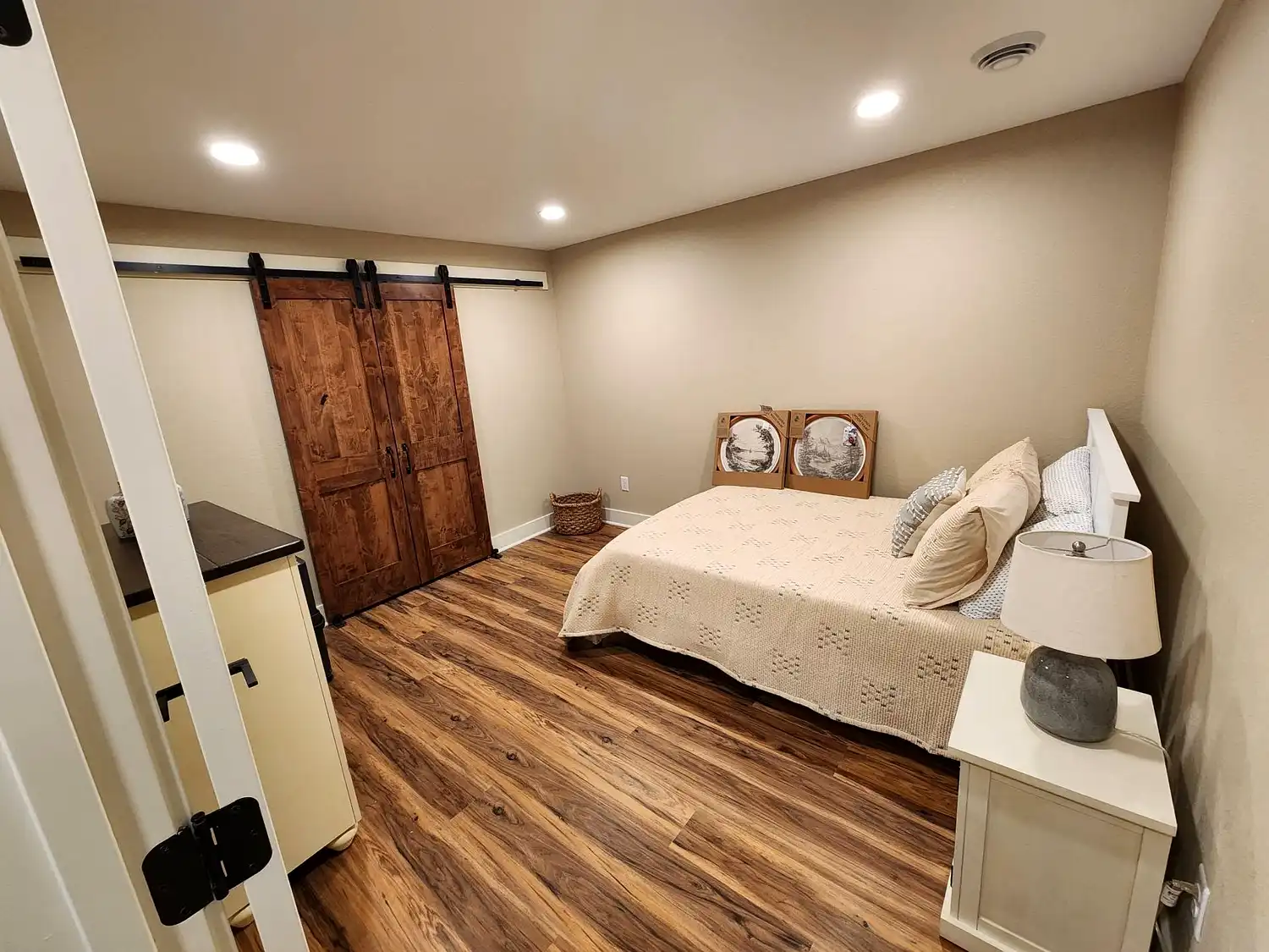 A beautifully finished basement with exposed black painted ceiling joists, crisp white walls, plush carpeting, and a cozy sitting area with electric fireplace and wall-mounted TV. Multiple rooms including a gym are visible, showing the full transformation of this Philadelphia basement.