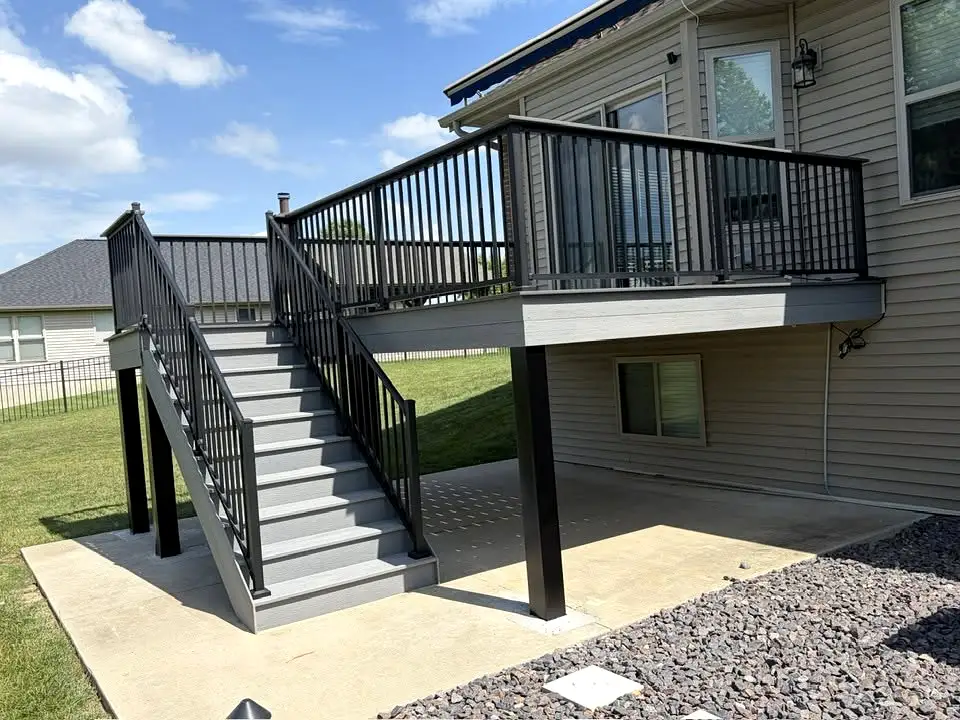 A magazine-worthy multi-level composite deck at dusk featuring a black pergola with string lights, separate dining and lounge zones, built-in step lighting, and lush landscaping with oversized planters. This two-tier deck renovation is the ultimate outdoor living upgrade for Philadelphia homeowners.