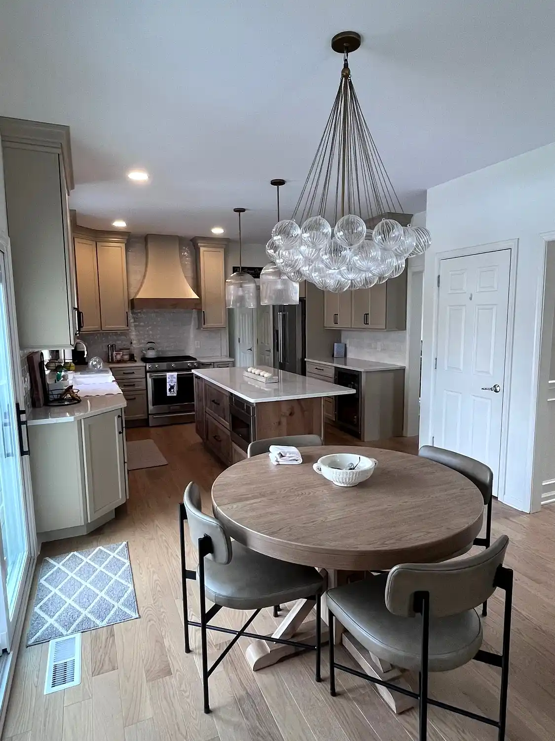 A spacious finished basement featuring a full wet bar with black granite countertops, dark cabinetry, mirrored backsplash, and an open lounge area with leather sectional seating. Light LVP flooring and recessed lighting make this an ideal entertainment space for Philadelphia homeowners.
